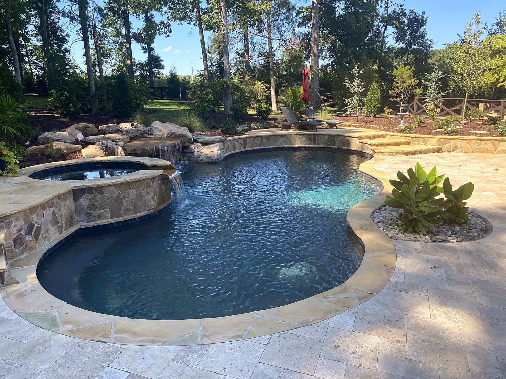 Freeform natural pool with rock waterfall, raised spa, and tropical landscaping